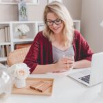 How to Build a Freelance Routine That Actually Sticks Woman smiling holding glass mug sitting beside table with macbook