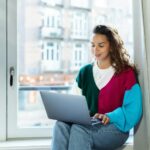 How to Market Yourself as a Freelancer Without Feeling Salesy A woman sitting on a window sill using a laptop