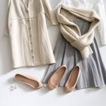O guarda-roupa cápsula perfeito para uma mulher tradicional: elegância intencional para sua vida doméstica. Flat lay of classic capsule wardrobe pieces: linen dress, cardigan, white blouse, neutral skirt, lea